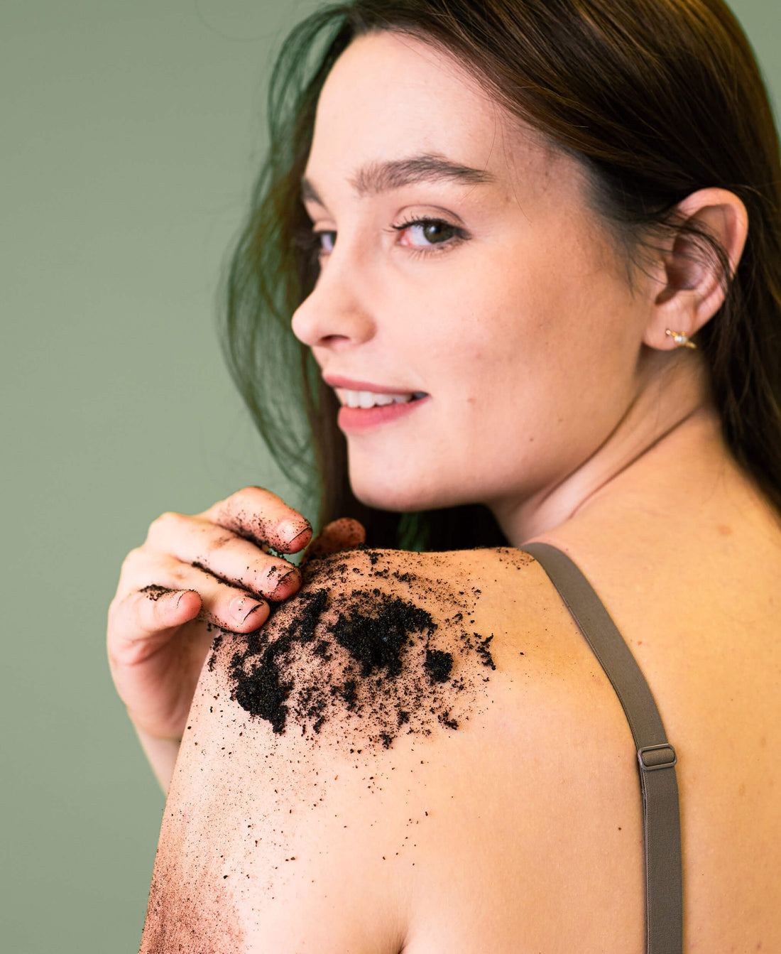 Woman applying Revived Peppermint Coffee Scrub on shoulder against green background