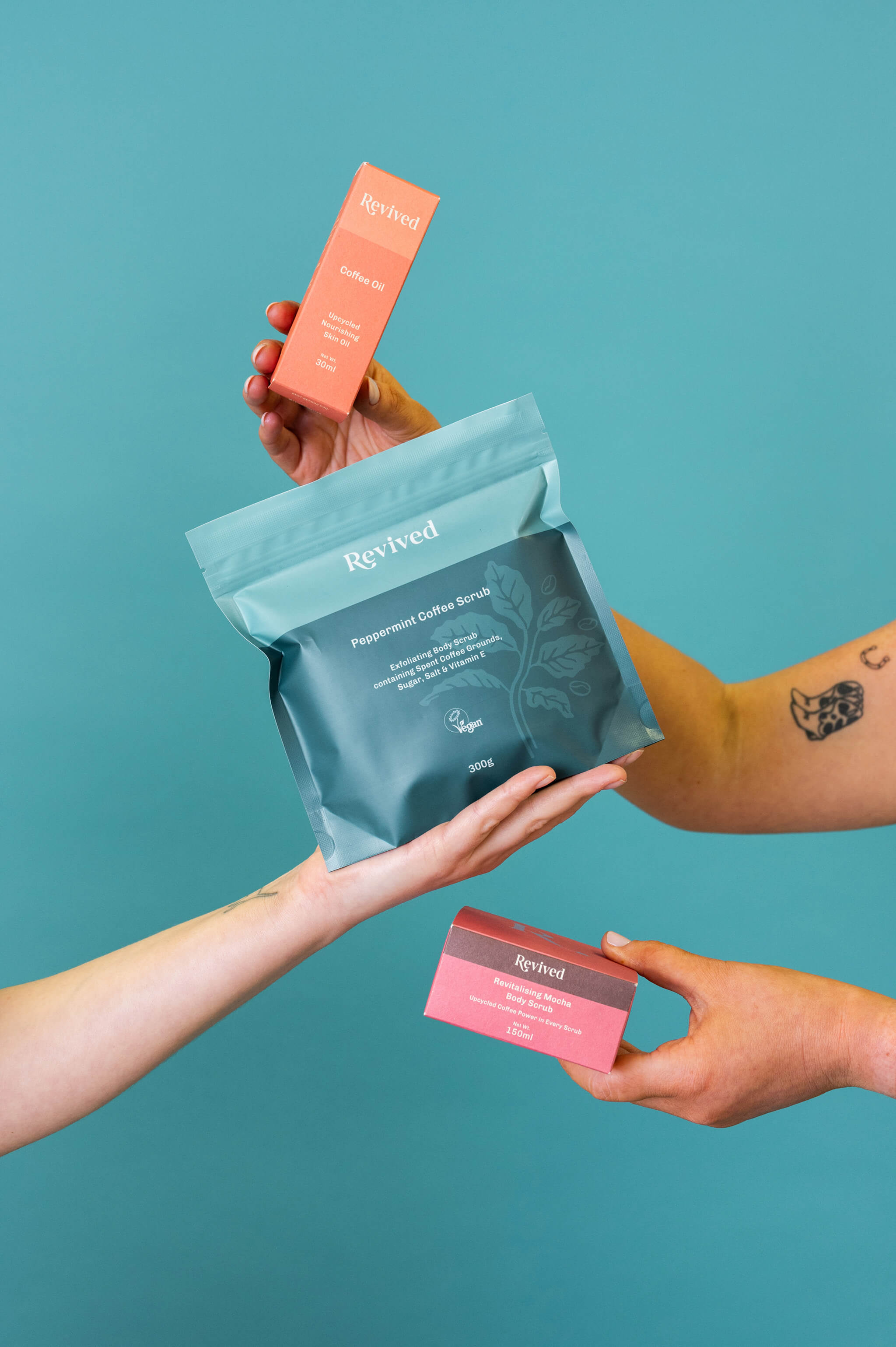 Revived coffee oil, peppermint scrub and mocha whipped scrub being held by several different hands to show them off.