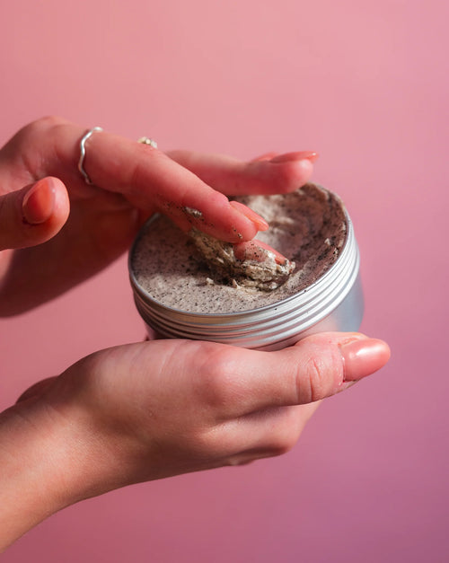 Person holding a tub of cosmetic product against a pink background