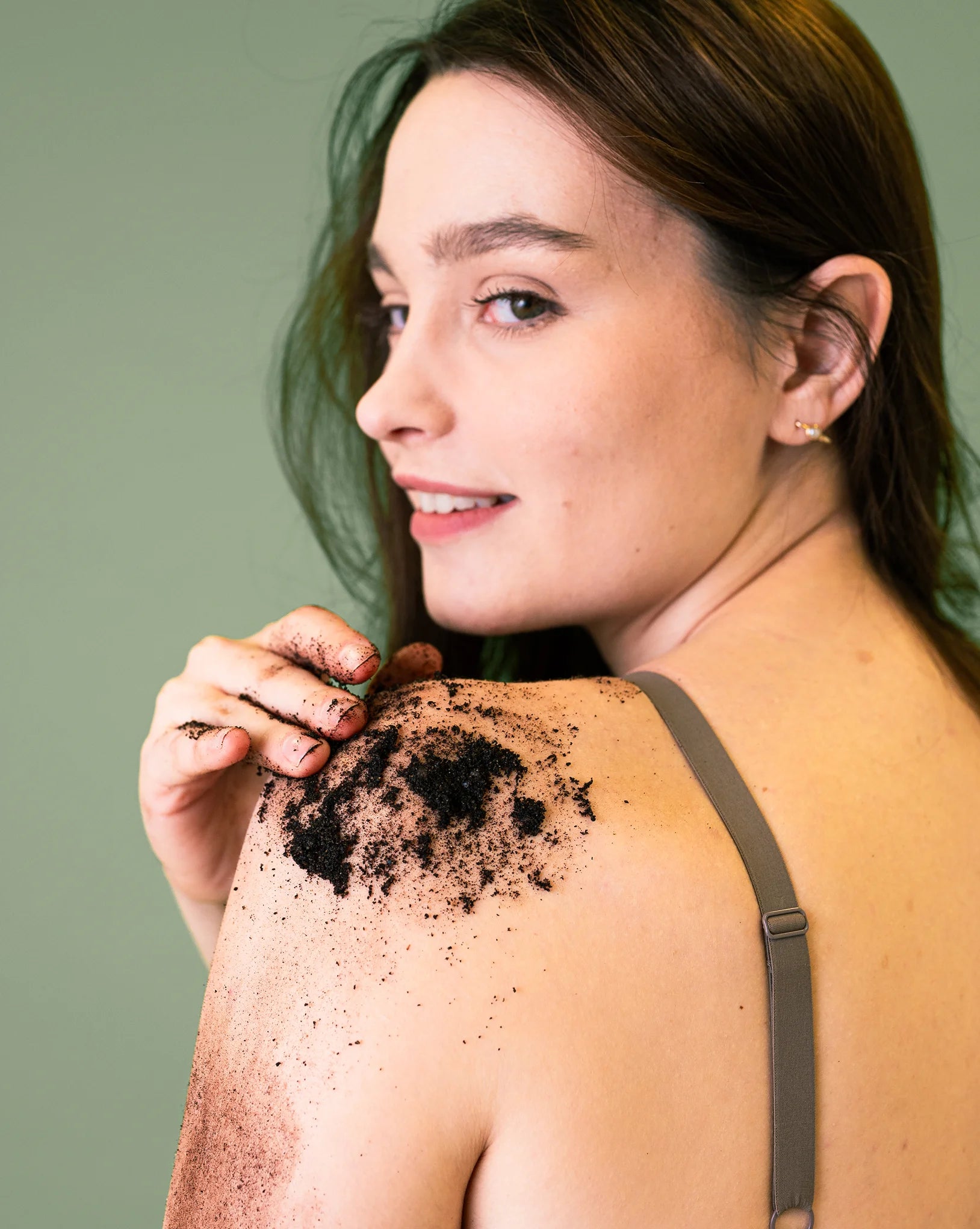Woman with coffee scrub on her shoulder against a green background