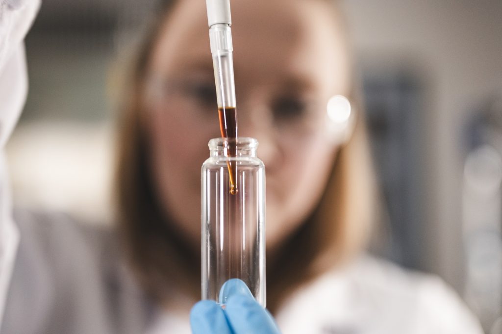 Person holding pipette with coffee oil dripping into test tube in lab