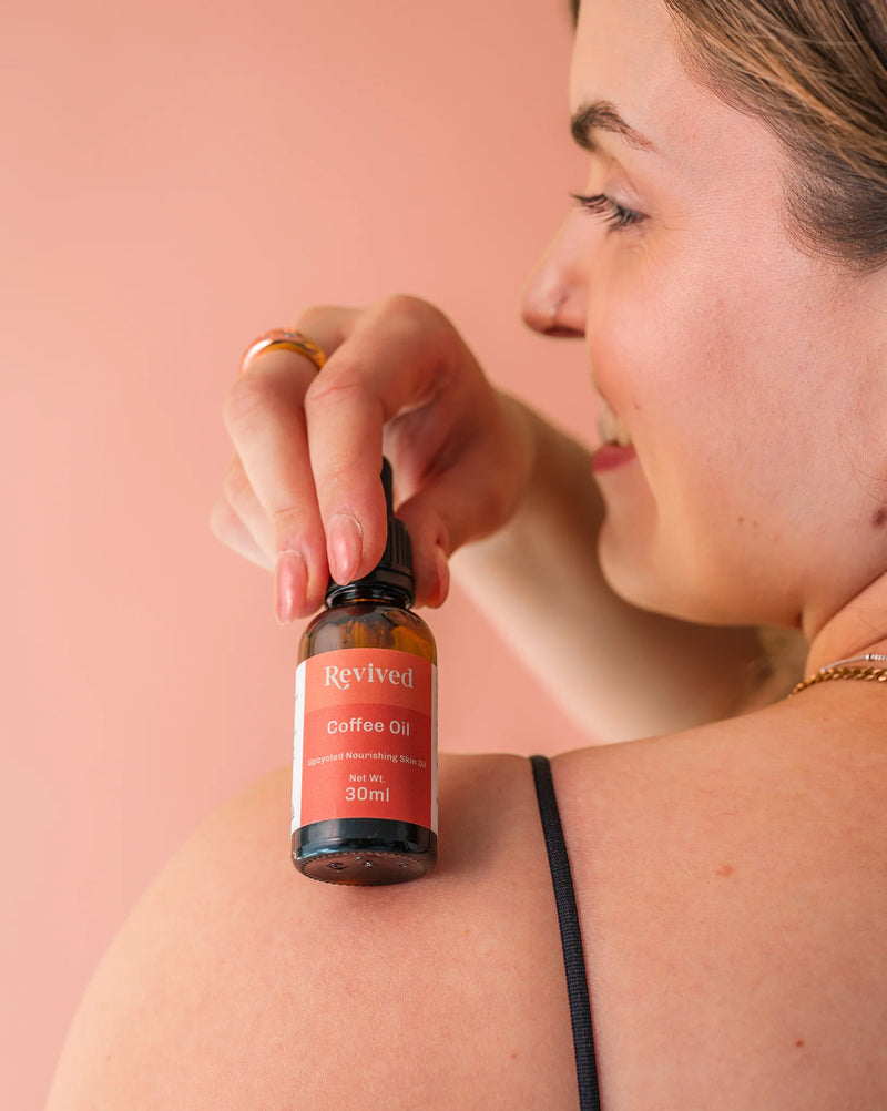 Woman holding a bottle of Revived Coffee Oil over her shoulder against a pink background