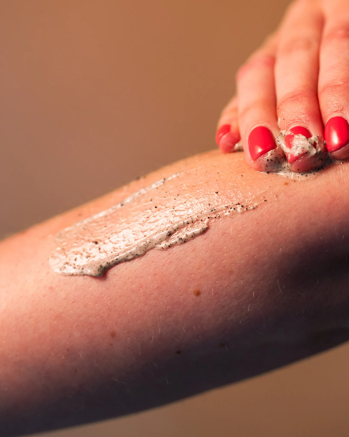 Hand applying Mocha scrub to a person's arm with a blurred background