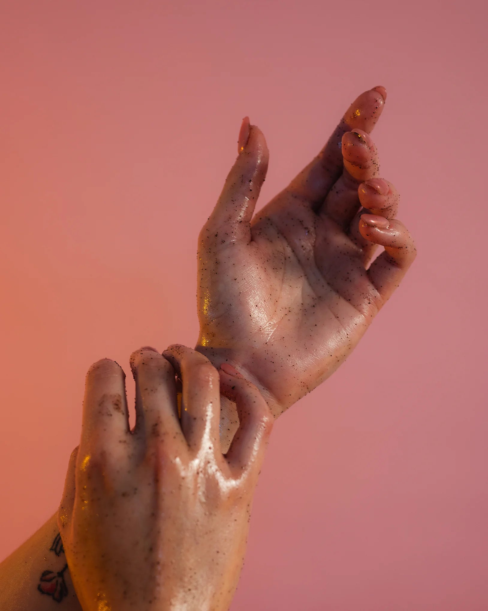 Close-up of two hands massaging coffee scrub with a pinkish-orange gradient background