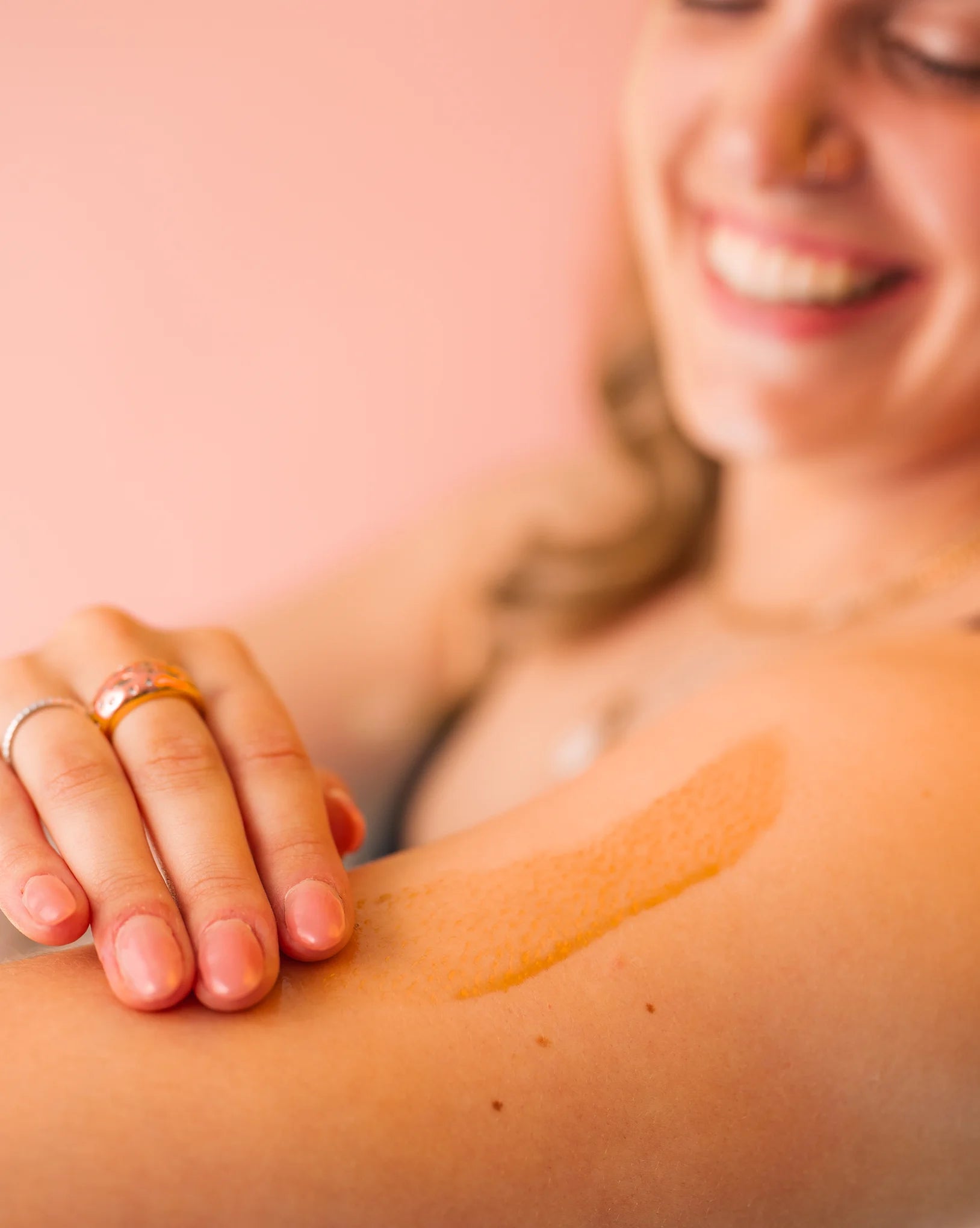 Woman applying Revived coffee oil to her arm with a brush against a pink background