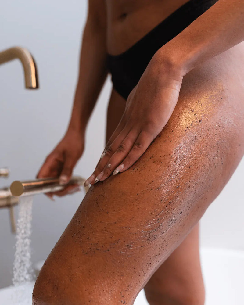 A close-up lifestyle shot of a person using whipped mocha body scrub on their leg, wearing black underwear. The leg shows the exfoliating and moisturising properties of this 2-in-1 body scrub.