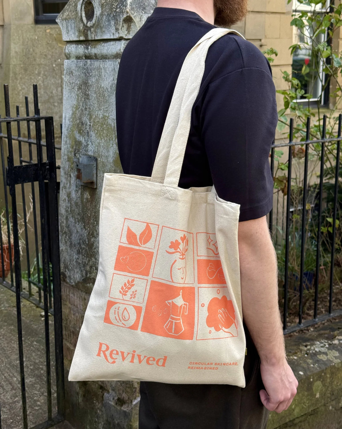 Person carrying a tote bag with 'Revived' icon mosaic branding and orange graphics.