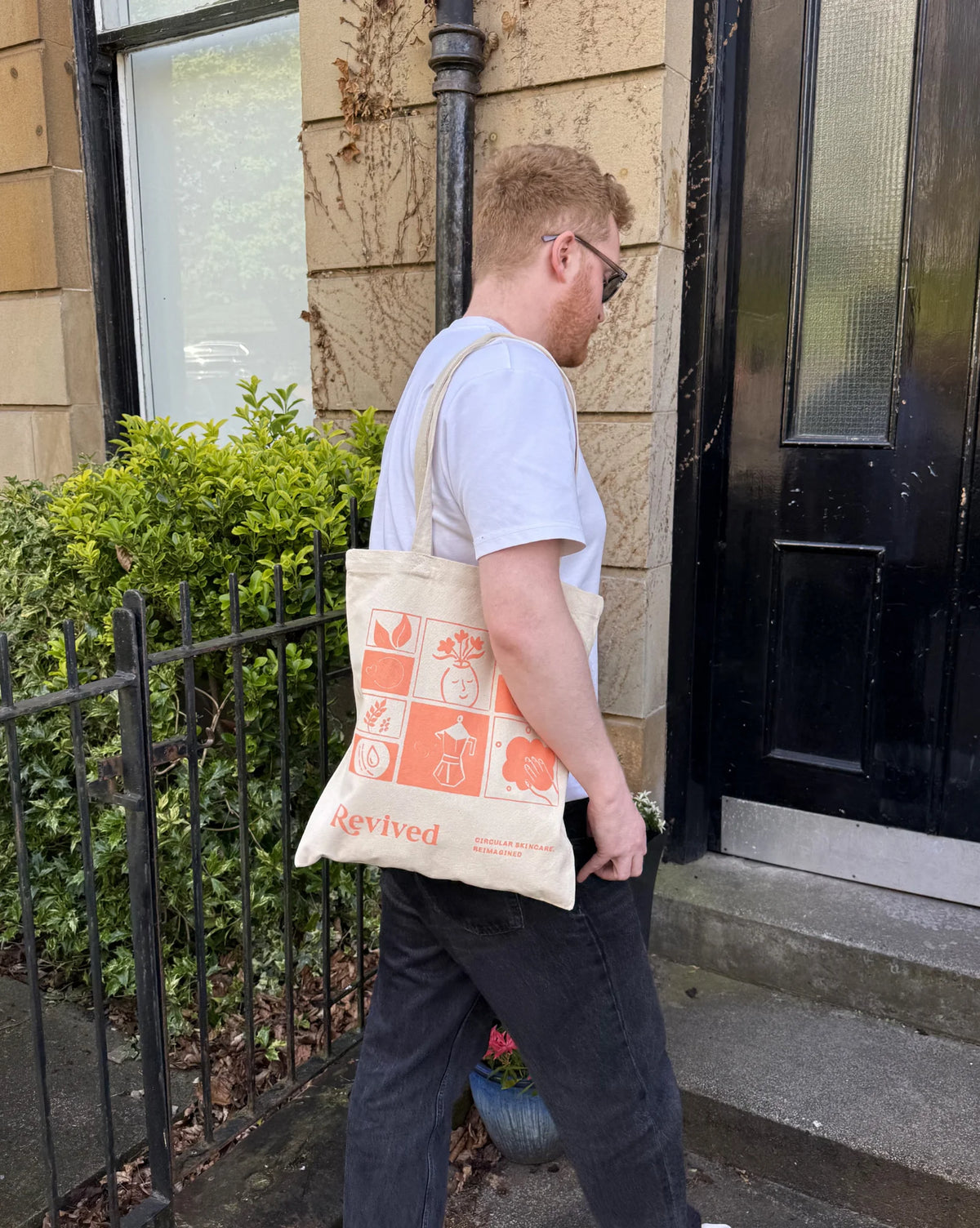 Person carrying a tote bag with orange graphics and text, walking outside a building.